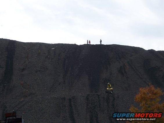 Dirt bike rider on a large coal pile with people on top