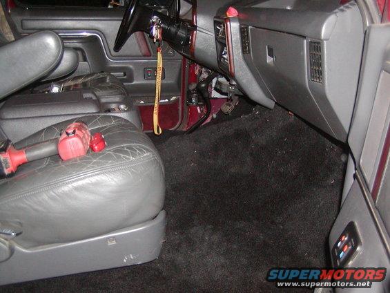 Interior shot of a vehicle's passenger side, showing cracked leather seat, black carpet, and dashboard with steering wheel and center console