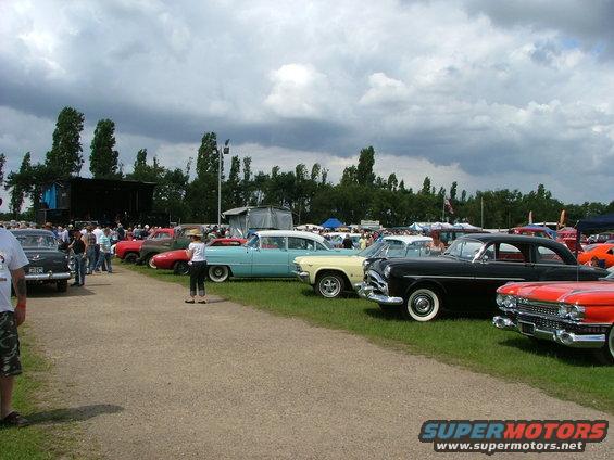 Cars parked in rows at an outdoor event with a stage in the background