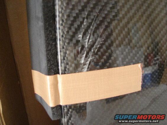 Carbon fiber panel secured with tan tape, showing a woven texture and plastic film