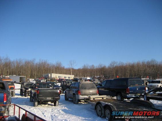 Snowy parking lot with many trucks and SUVs, some on trailers