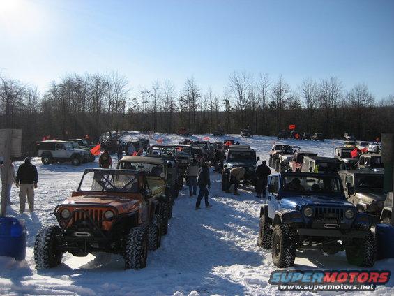 Line of off-road vehicles parked in snow, with trees and a clear blue sky