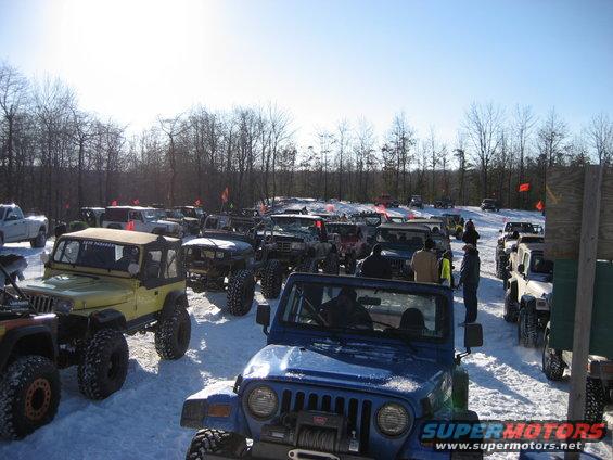 Many off-road vehicles parked in a snowy field with trees in the background