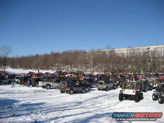 Many SUVs and trucks parked in a snowy lot under a clear blue sky
