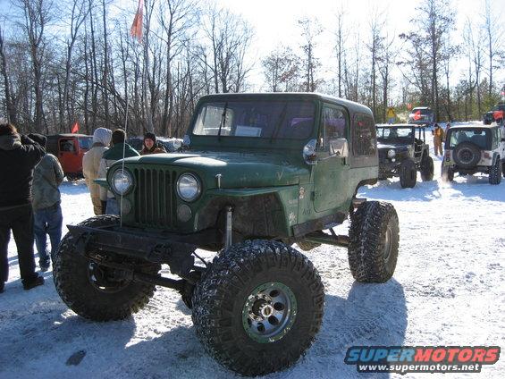 Green lifted Jeep with large tires in snow, other off-road vehicles in background