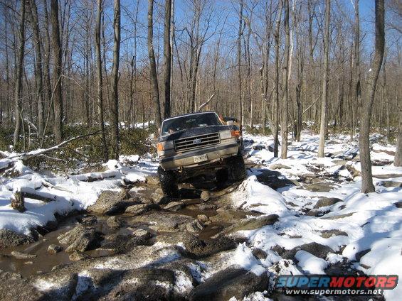 1991 Ford Bronco navigating a rocky, snowy trail through bare trees