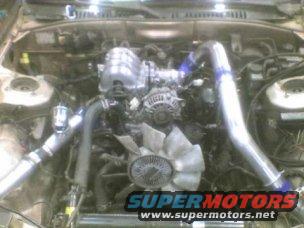 Engine bay with large intercooler piping and a fan, SuperMotors.net logo visible