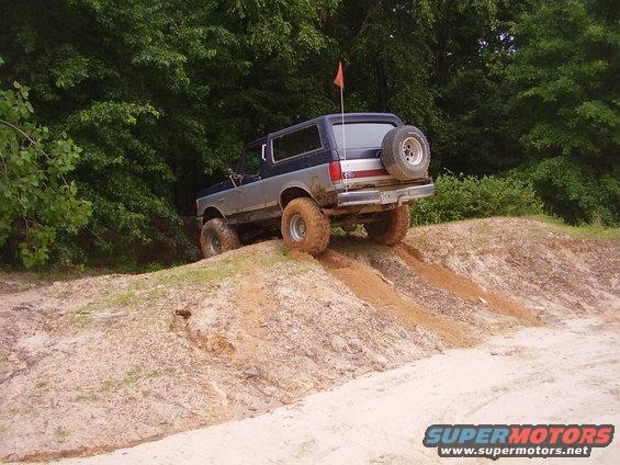 1991 Ford Bronco climbing a dirt hill with trees in background