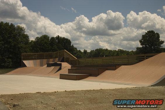 Wooden skate park ramps with concrete flat ground and trees in background