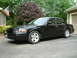 2002 Ford Crown Victoria - A black 2002 Ford Crown Victoria is parked in front of a garage with an American flag visible.