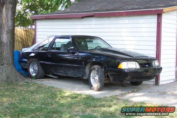 Black Ford Mustang parked next to a garage. Hood scoop is visible
