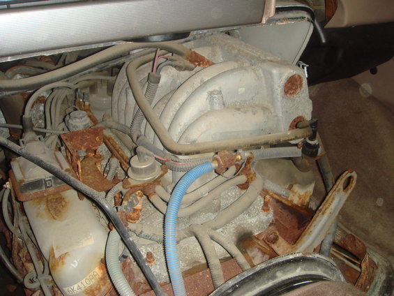 Close-up of a rusty engine bay with various hoses and components visible. Part number 6K410AA is partially visible on a white plastic component