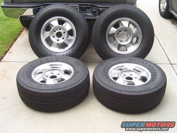 Four tires and rims on concrete, with truck bumper visible