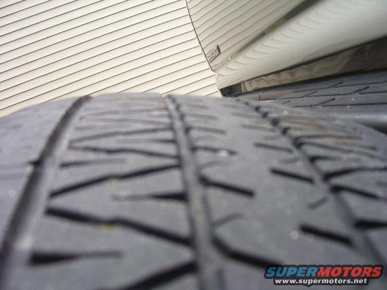 Close-up of a tire tread with a shiny vehicle body and siding in the background. Text 'SUPERMOTORS' visible