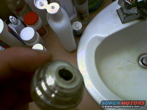 Close-up of a chrome faucet handle part over a sink with toiletries