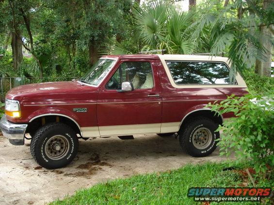 Maroon and tan 1993 Ford Bronco parked on a dirt driveway, side view