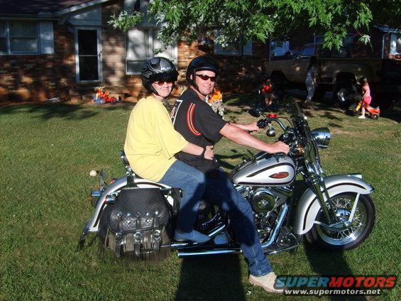Silver motorcycle with two riders, side view. Motorcycle has leather saddlebags