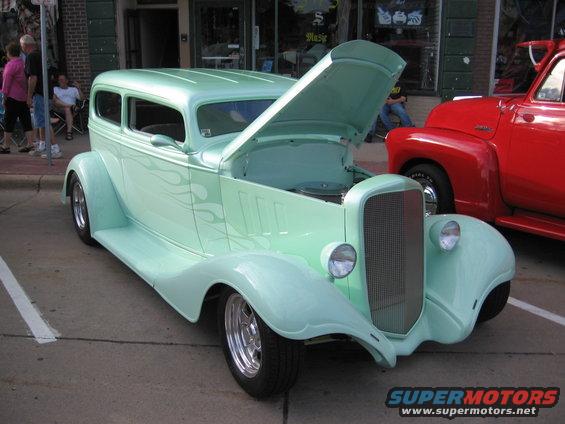 mint green hot rod sedan with hood open, parked next to red pickup truck