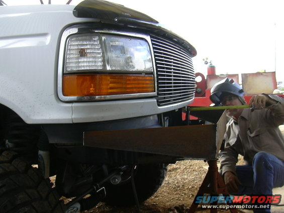 Guy in welding mask measures custom bumper on white Ford truck. Grille and headlights visible