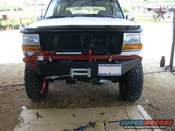 Front view of a 1995 Ford Bronco with a custom bumper, winch, and Hi-Lift jack mounted on it. Texas license plate visible