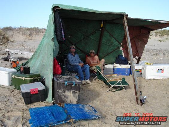 Beach shelter with two men, coolers, and chairs