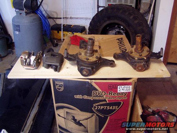 Two brake calipers and two steering knuckles on a wooden shelf above a TV box