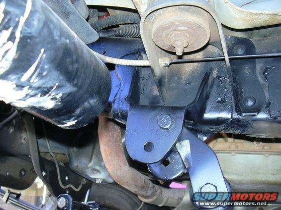 Close-up of a custom suspension bracket bolted to a vehicle's frame, with exhaust pipe visible