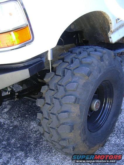 Close-up of a large off-road tire on a lifted truck, showing suspension components and part of the headlight
