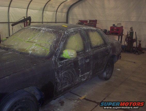 Black 1998 Ford Crown Victoria in a garage, prepped for paint with masking tape on windows