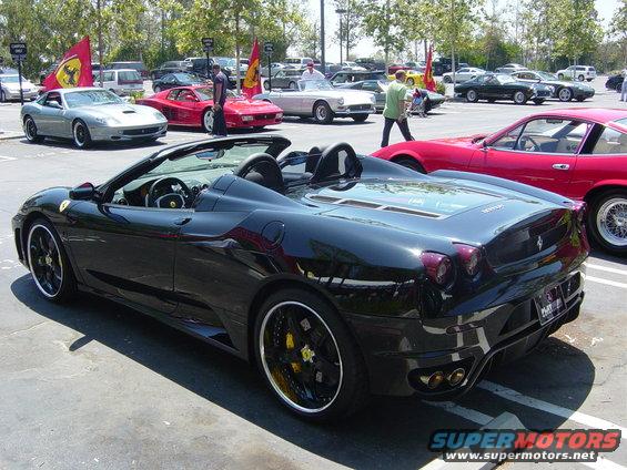 Black convertible sports car with custom wheels and yellow brake calipers, viewed from the rear three-quarter angle