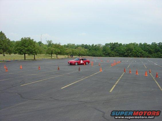 Red sports car navigating a cone course in an empty parking lot