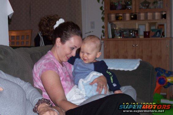 Woman holding a baby on a couch, with a shelf unit in the background. Date stamp reads 12/31/2005