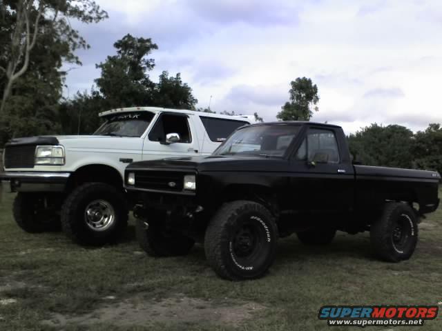 White 1995 Ford Bronco and black pickup truck parked side-by-side