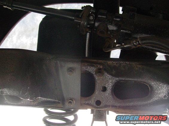 Close-up of vehicle frame with suspension spring visible. Steering linkage is also in view