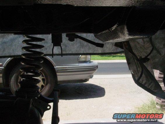 Silver car's front fender and wheel seen from below, with suspension parts in the foreground