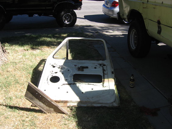 Car door lying on grass next to a black SUV and a yellow truck