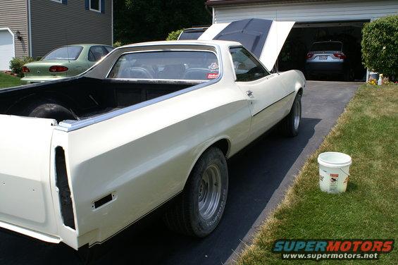 White 1972 Ford Ranchero with hood open, parked in driveway next to a green sedan and a car in garage