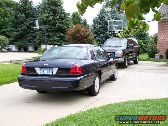 Dark blue 2003 Ford Crown Victoria parked on driveway, rear view. Another black SUV is behind it