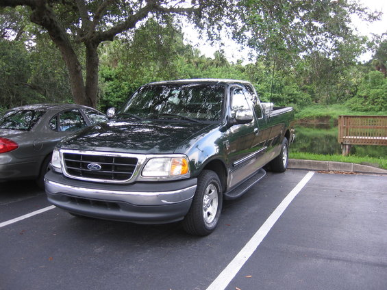 Dark green Ford F-150 pickup truck parked next to a gray sedan