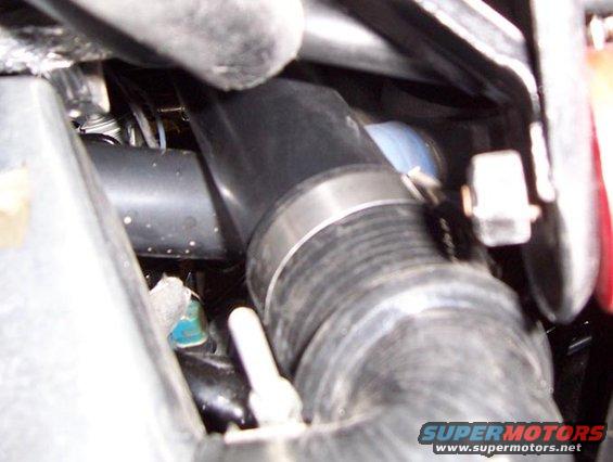 Close-up of a metal hose clamp on a black rubber hose, with other engine components visible