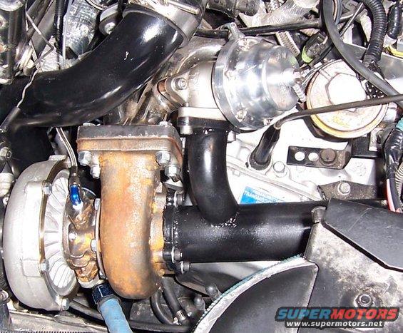 Turbocharger with rusty exhaust manifold and black intake pipe, engine bay detail