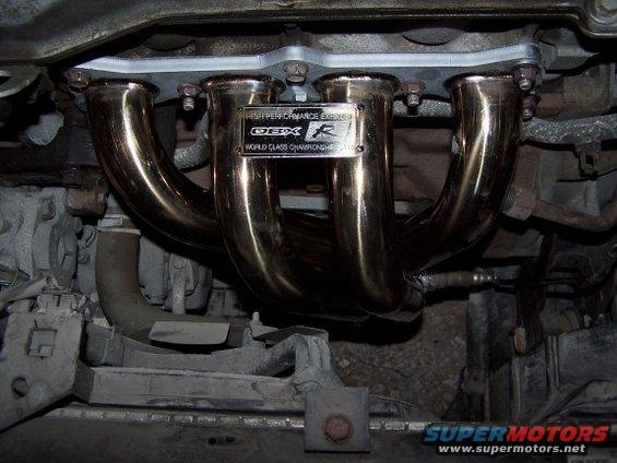 Aftermarket exhaust manifold with 'OBX R' and 'World Class Championship' text on a metal plate