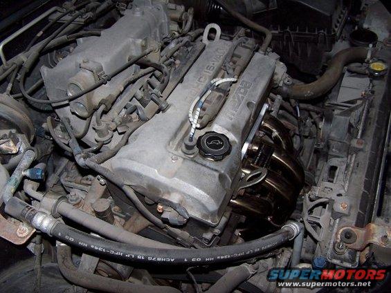 Mazda engine with exhaust manifold and hoses. The engine cover has "MAZDA" text
