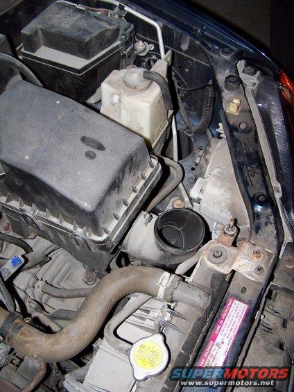 Engine bay with air intake, coolant reservoir, and radiator visible. Some text on radiator warning sticker