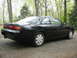 1995 Nissan 240SX - This black 1995 Nissan 240SX coupe is viewed from its rear-right side, with a wooded area behind it.
