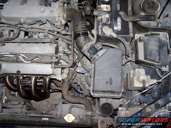 Engine bay with "MAZDA 16-VALVE" on the valve cover and a custom exhaust manifold
