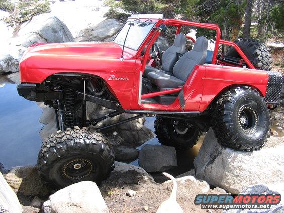 Red 1970 Ford Bronco with off-road modifications on rocks near water