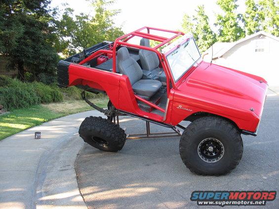 Red 1970 Ford Bronco modified with roll cage and oversized off-road tires, lifted suspension