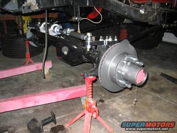 Undercarriage of a vehicle on jack stands, showing suspension and brake assembly