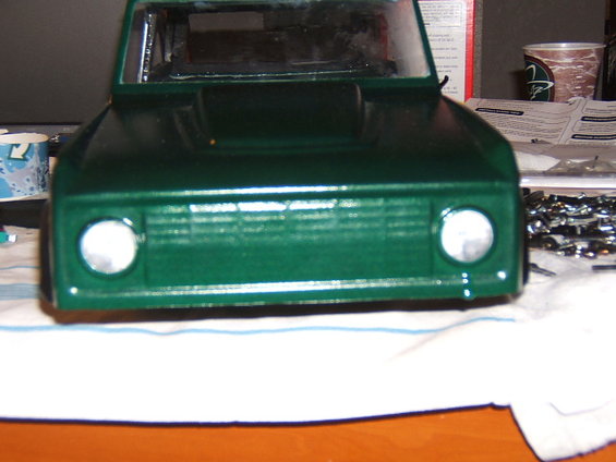 Green toy truck body with horizontal grille and round headlights, viewed from the front